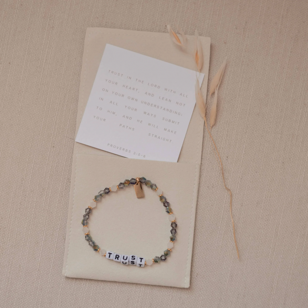 Bracelet with 'TRUST' beads on a beige card with a letter, on a beige surface