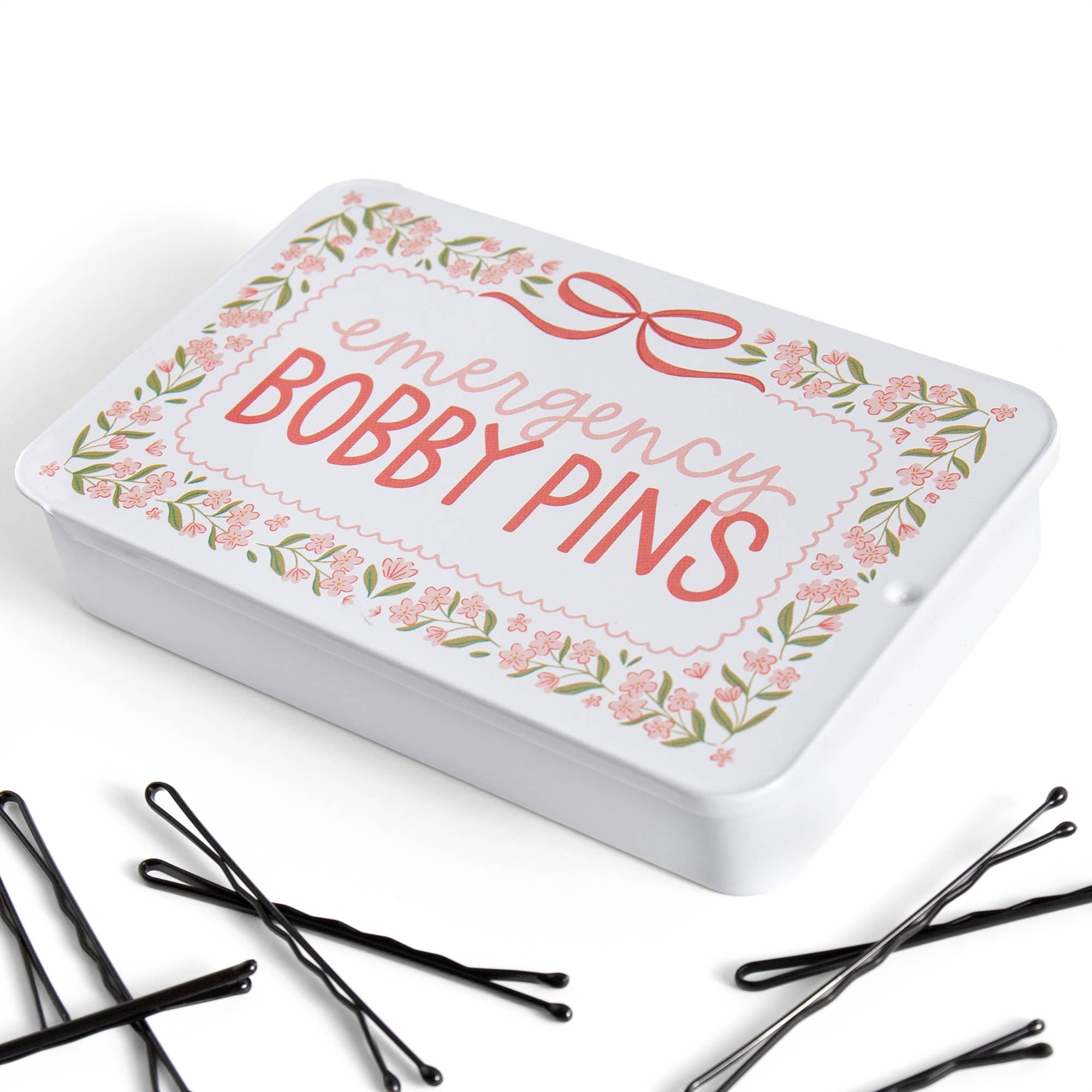 White tin labeled 'Emergency Bobby Pins' with decorative border, surrounded by black bobby pins on a white background.