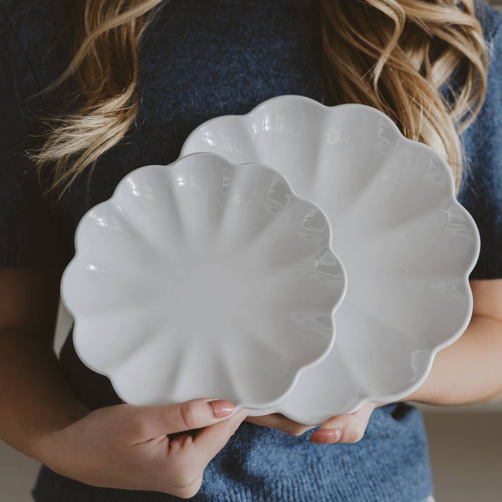 Person holding a white scalloped-edge ceramic dish