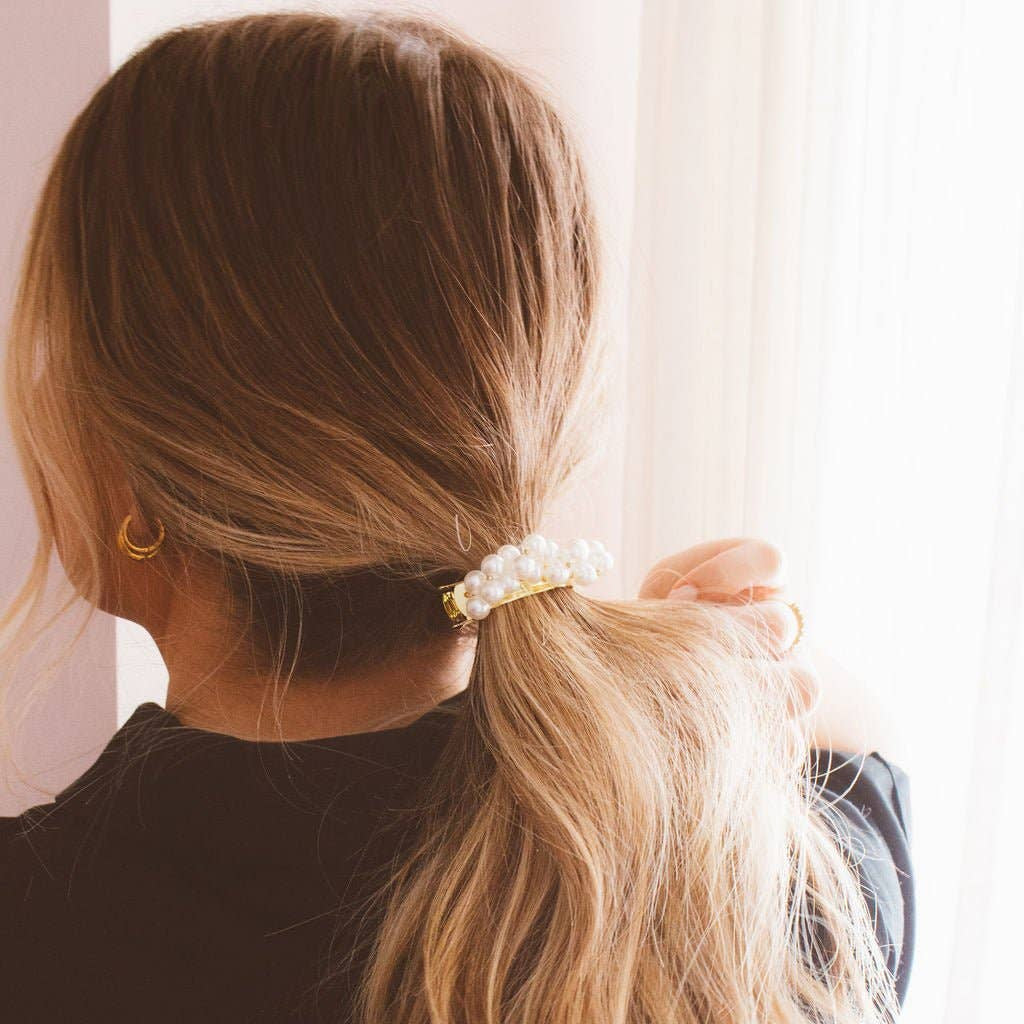 Person with long blonde hair tied back with a decorative hair tie, wearing a black top.