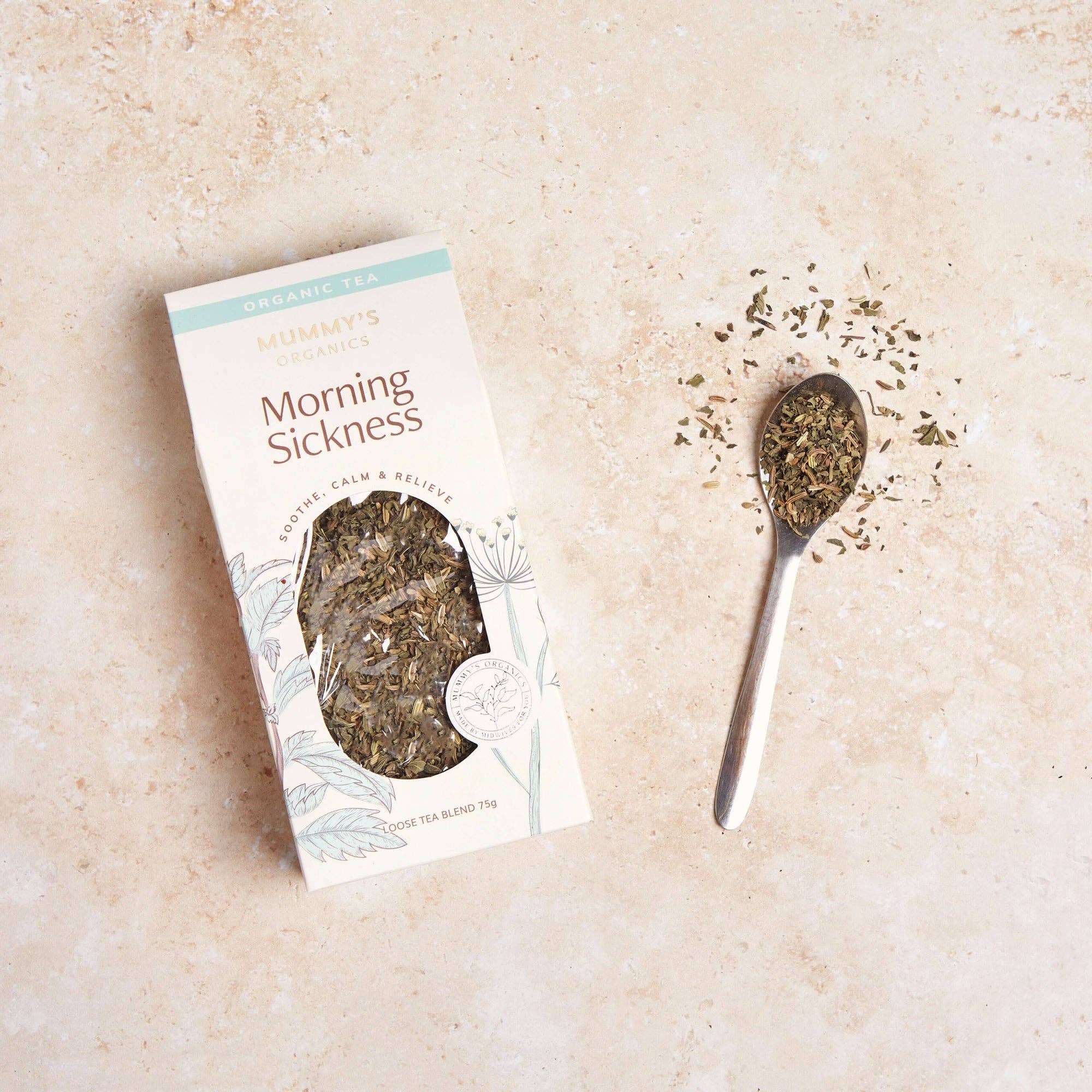 A package of Mummy's Organic Morning Sickness herbal tea sits on a light beige textured surface next to a small metal spoon filled with loose dried tea leaves.