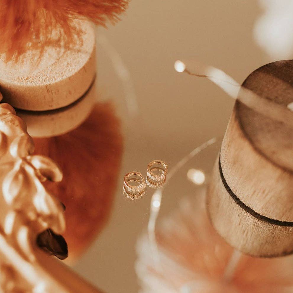 Gold hoop earrings on a wooden stand with a warm, blurred background