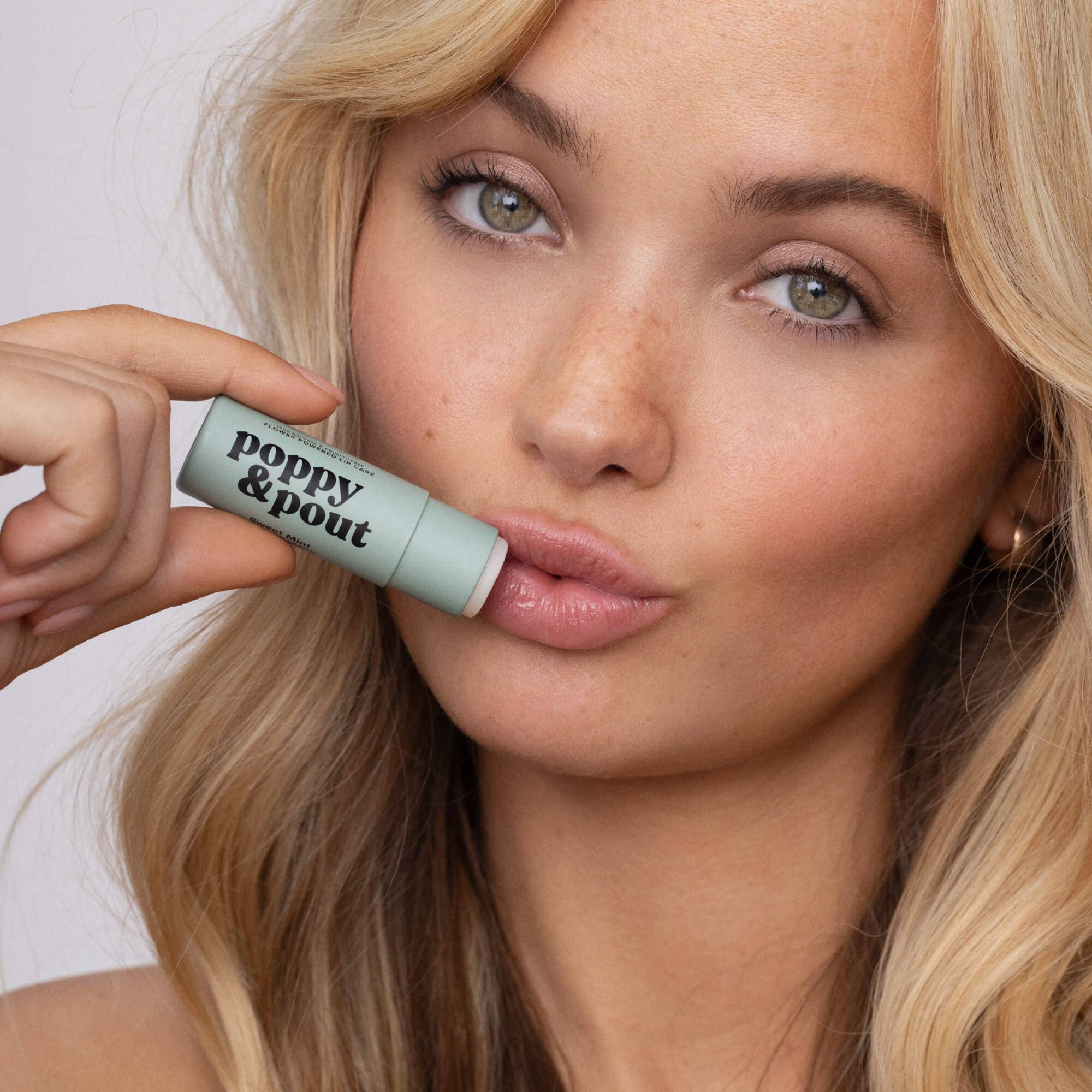 Woman holding a 'poppy & pout' lip balm close to her lips.