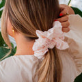 Person with a pink scrunchie in their hair, wearing a white top.