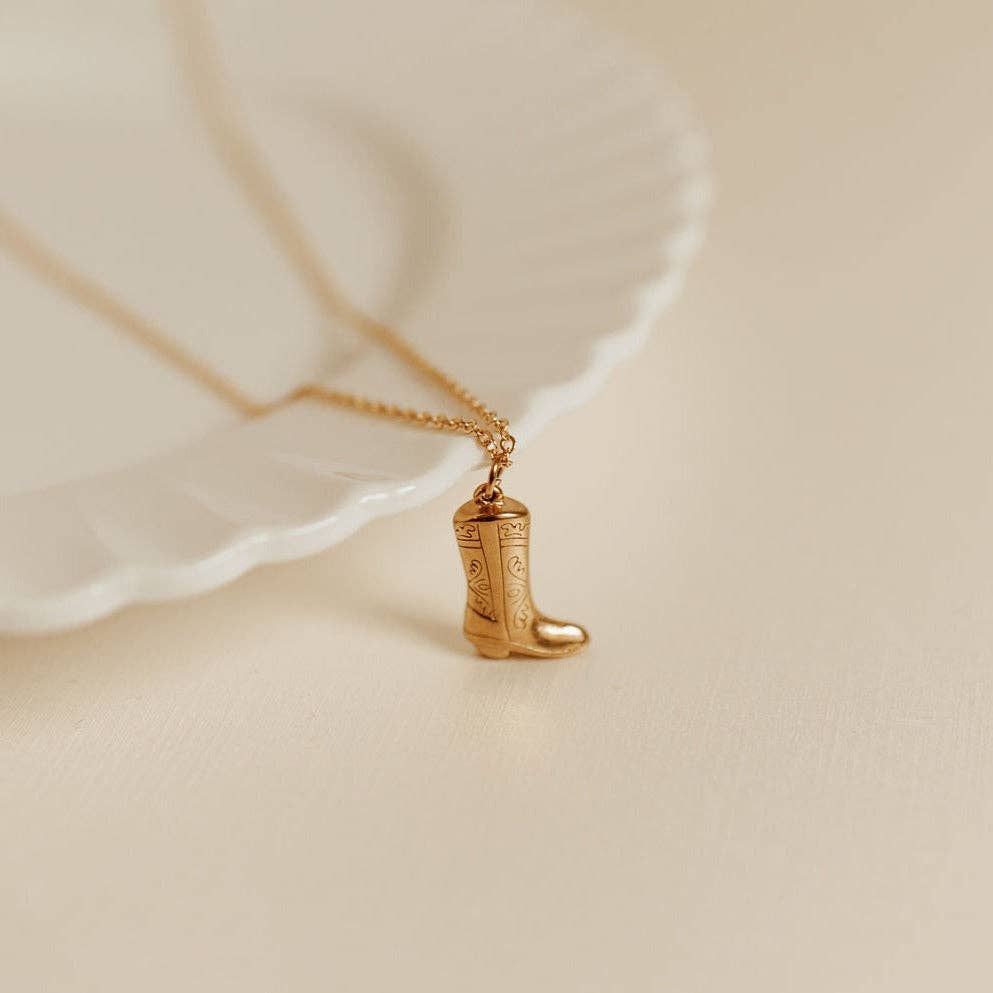 Gold boot-shaped pendant on a chain against a beige background