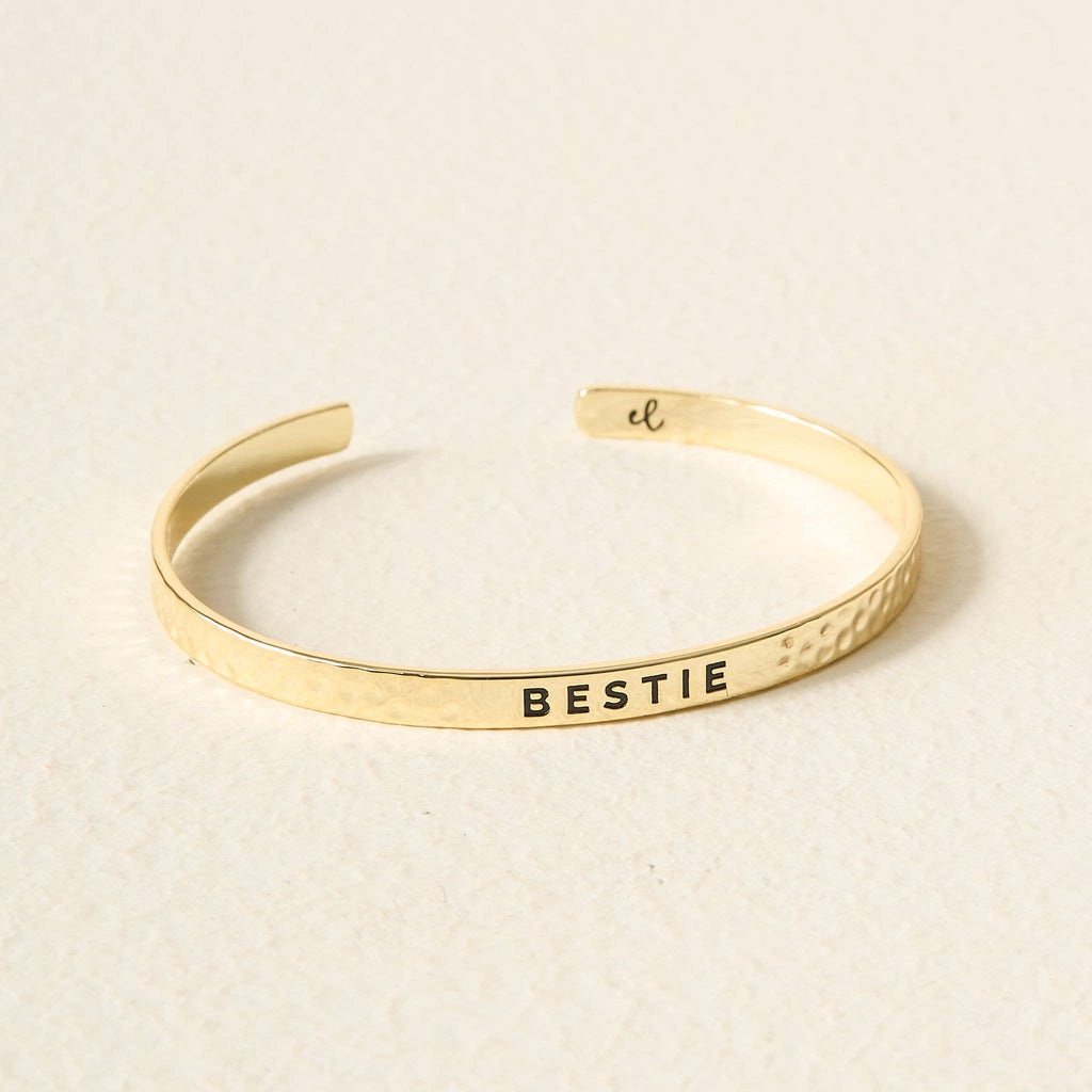 Gold bracelet with 'BESTIE' engraving on a beige background