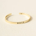 Gold bracelet with 'BESTIE' engraving on a beige background