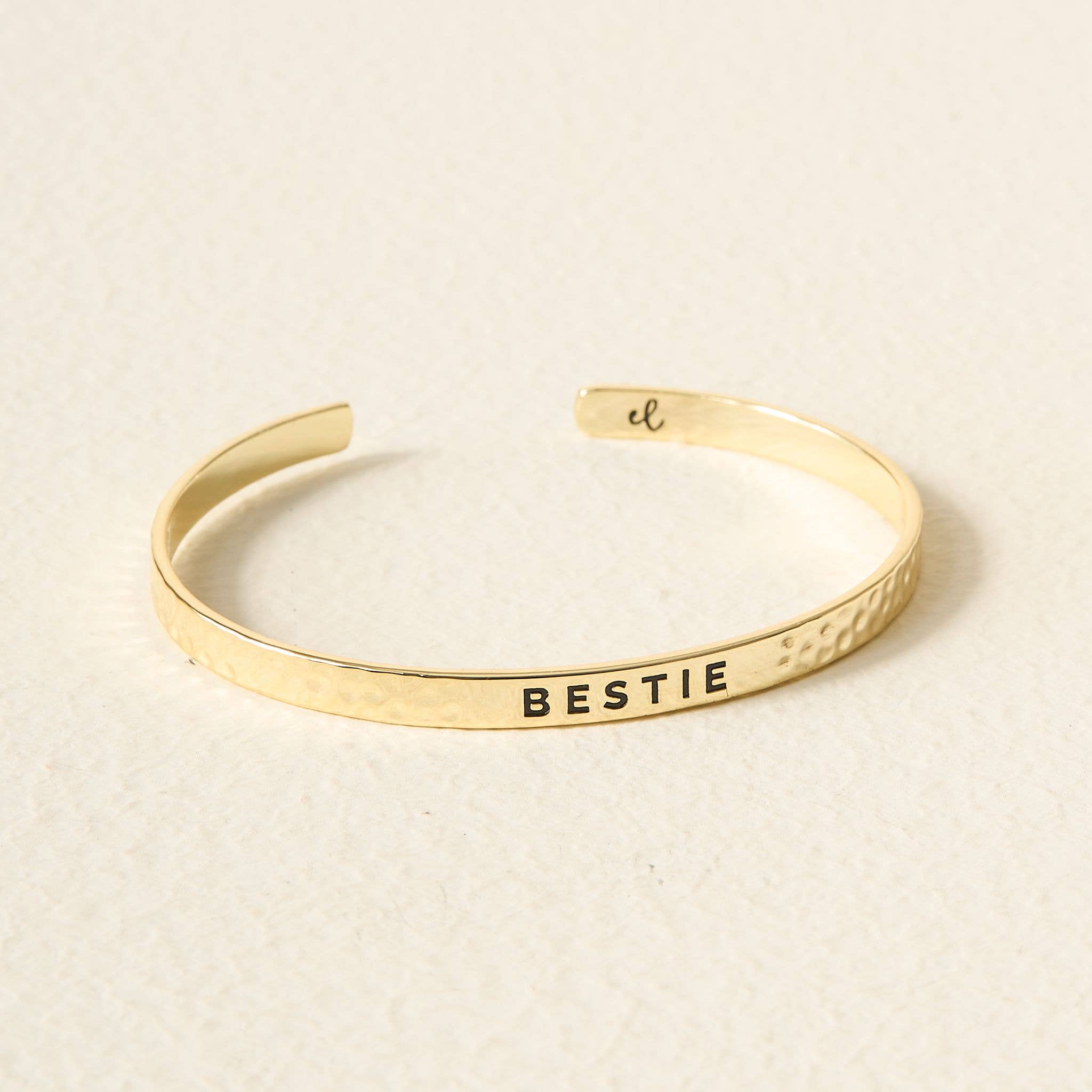 Gold bracelet with 'BESTIE' engraving on a beige background