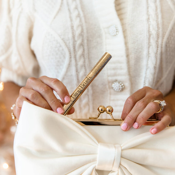 Person holding a white clutch with a large bow, wearing a white textured cardigan.