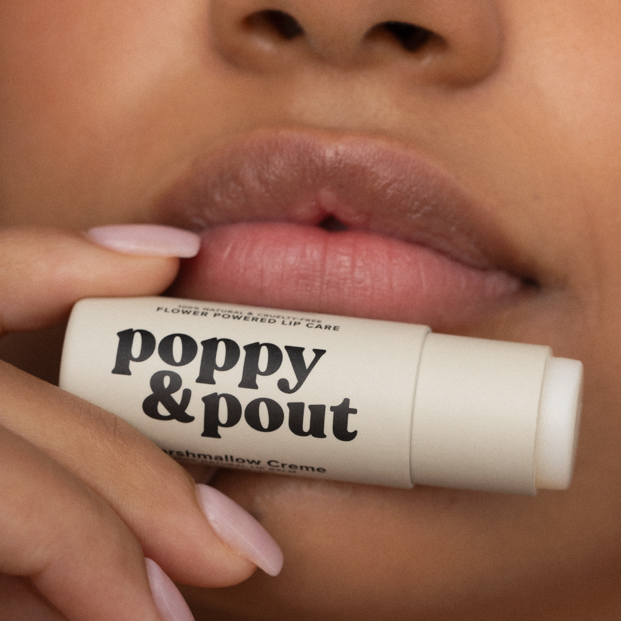 Lip balm stick with 'poppy & pout' branding held by a person's hand.