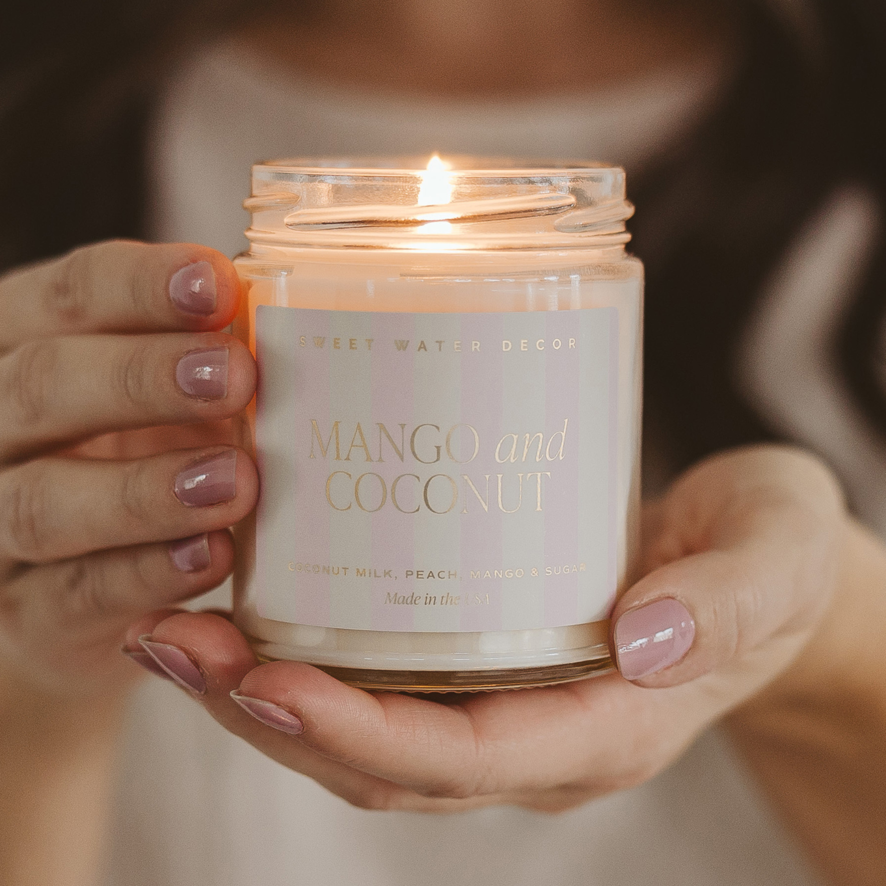 Hand holding a 'Mango and Coconut' scented candle with a blurred background