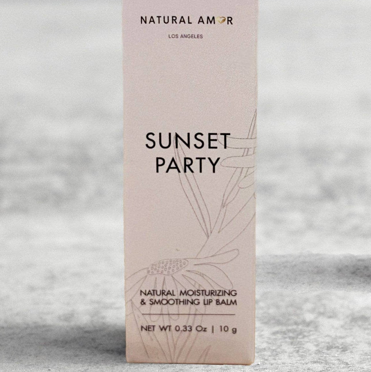 Lip balm and packaging labeled 'Sunset Party' on a light surface with dried flowers.