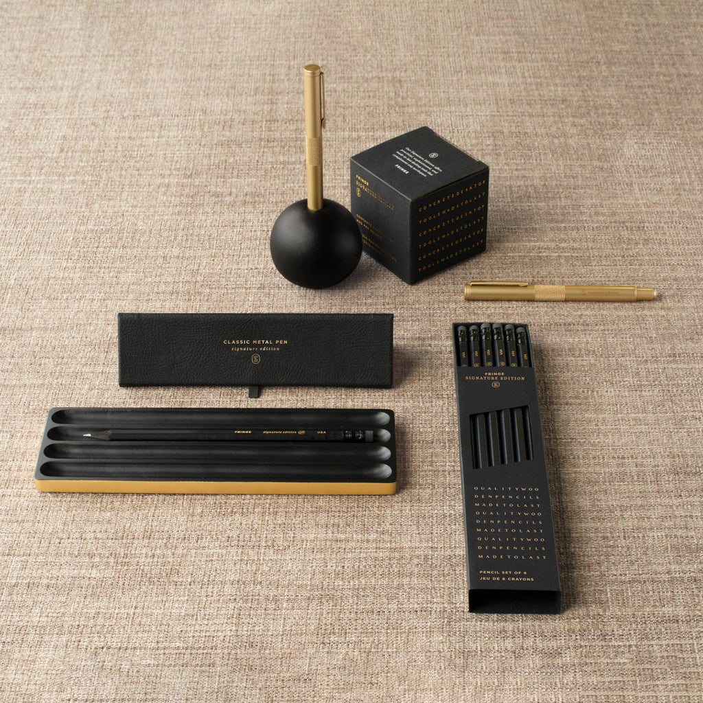 Collection of black and gold pens and accessories on a textured surface