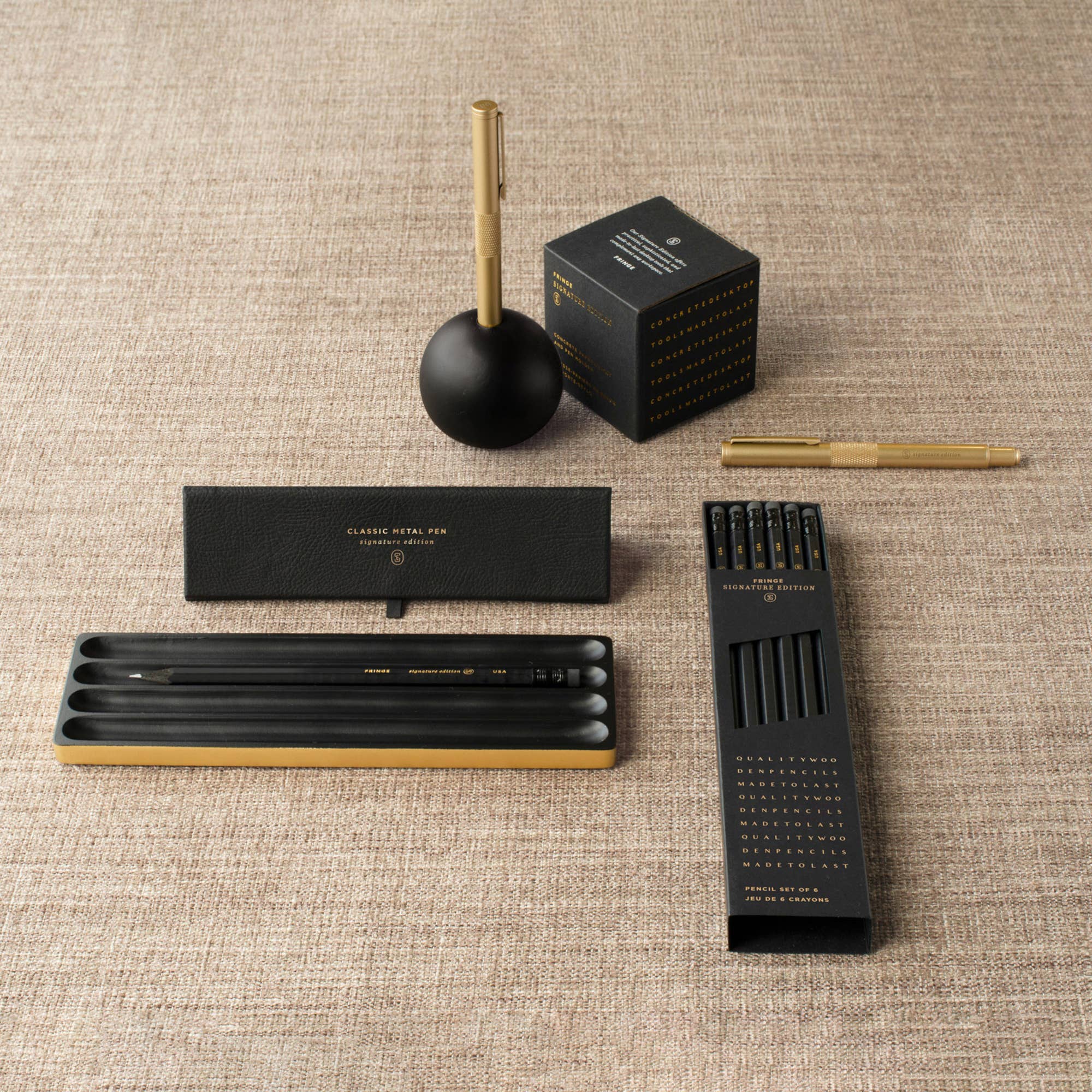 Collection of black and gold pens and accessories on a textured surface