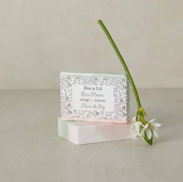 Bar of soap with a floral design label next to a rice flower on a neutral background