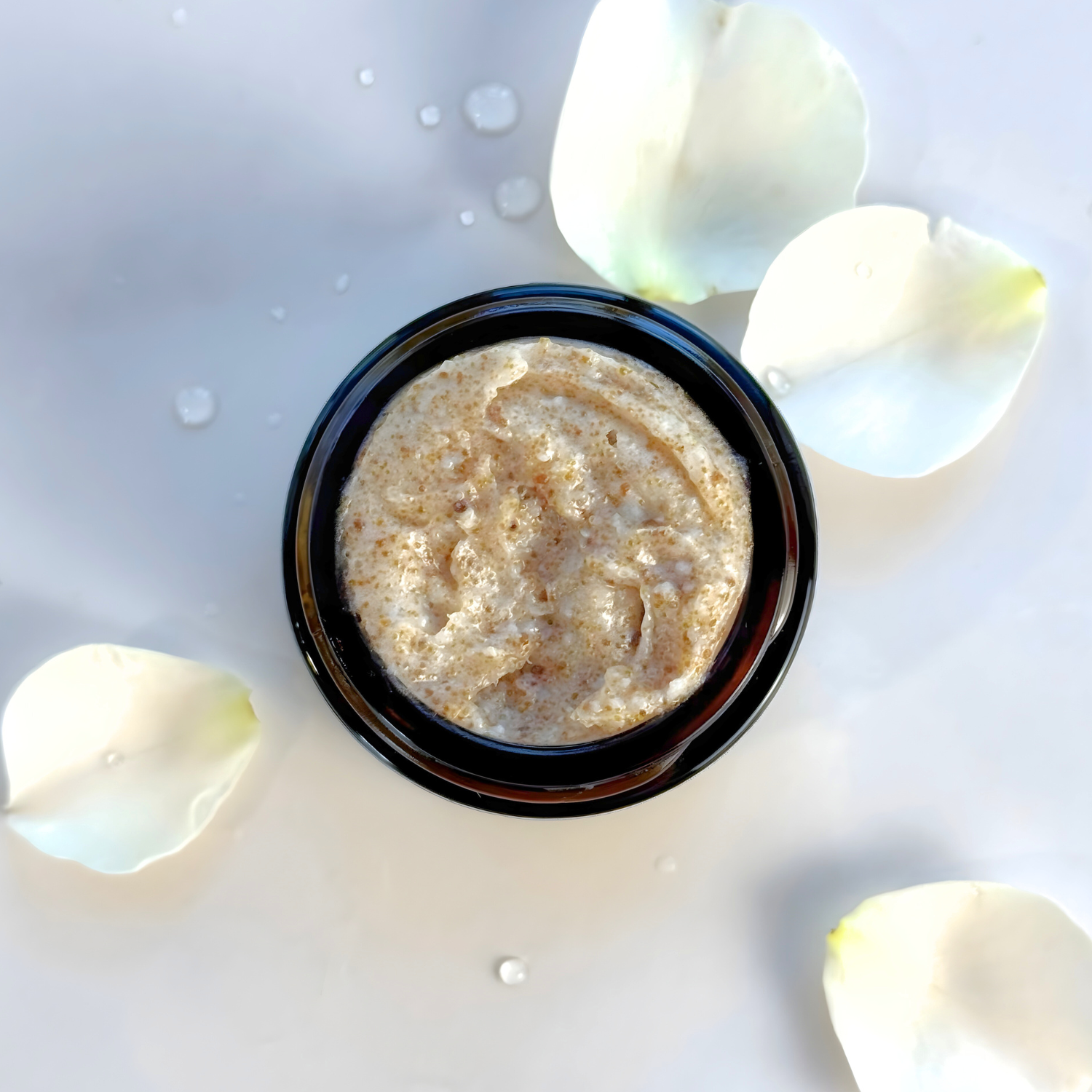 Small container of beige cream with white petals on a light background
