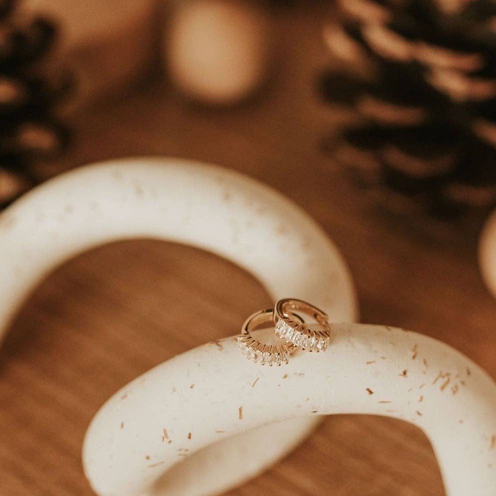 Gold ring on a white ceramic object with blurred pinecones in the background