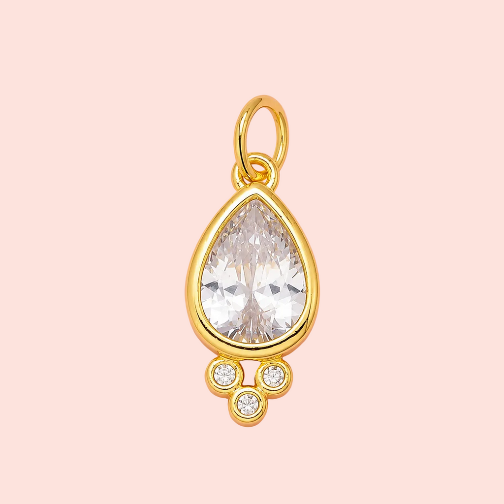 Gold pendant with a large clear gemstone on a pink background