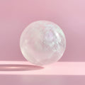 Hand holding a translucent, iridescent crystal ball against a neutral background