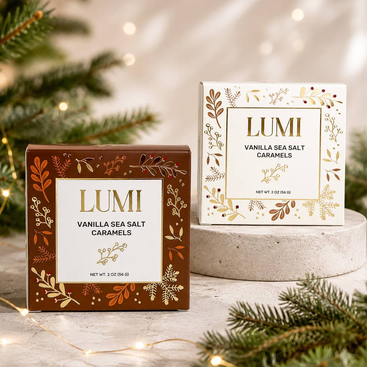Two LUMI Vanilla Sea Salt Caramels boxes displayed on a stone pedestal with holiday greenery and warm string lights in the background.
