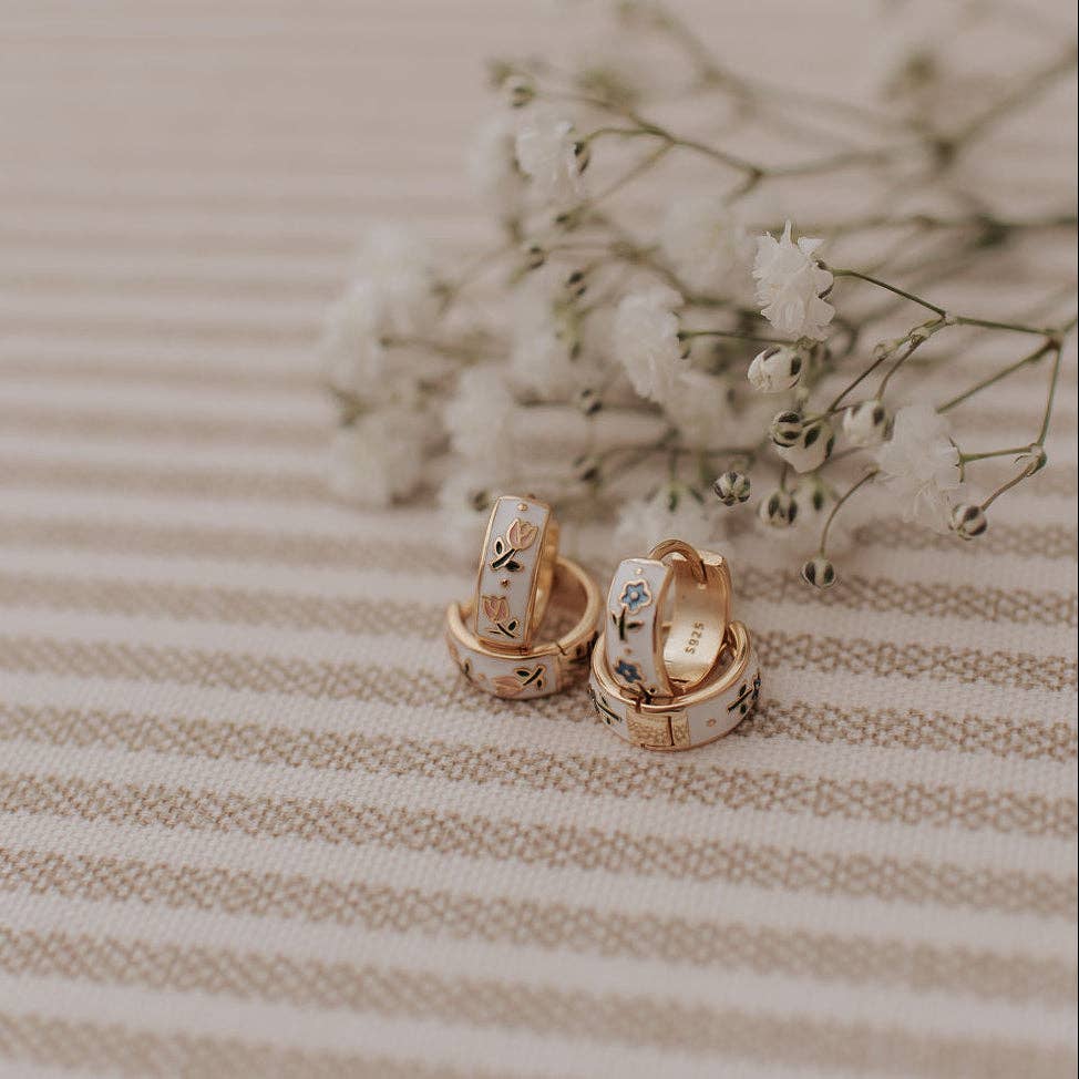 Gold hoop earrings with floral designs on a striped fabric background