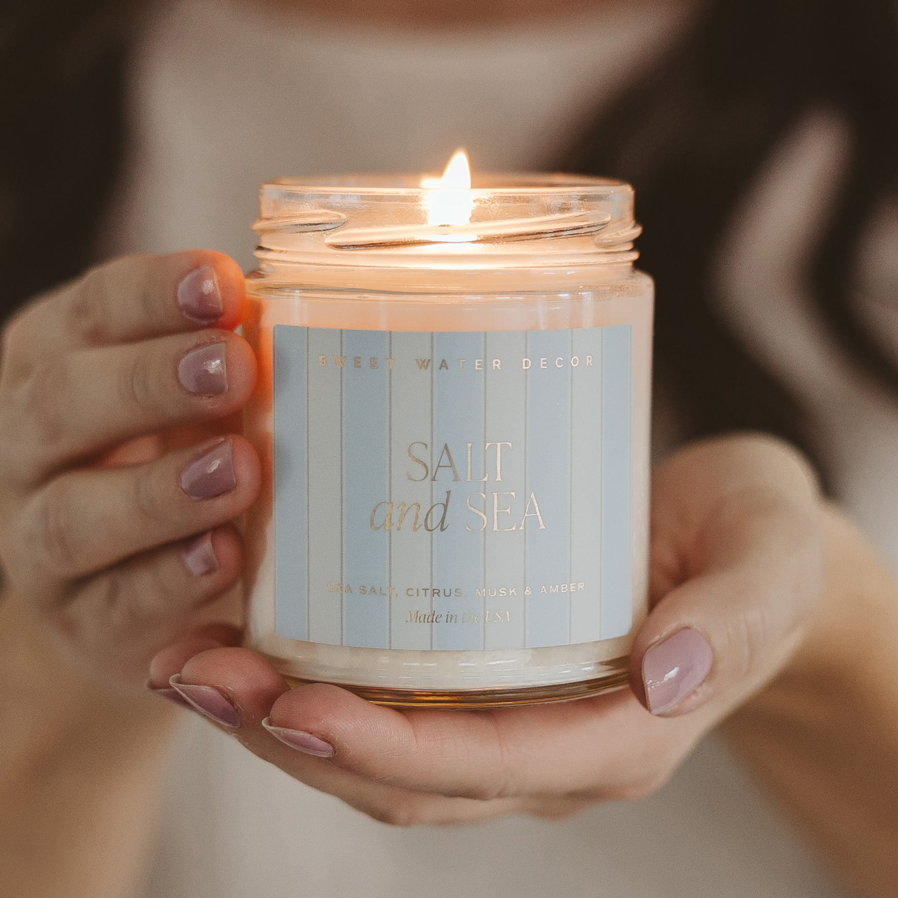 Candle labeled 'Salt and Sea' held in hands with a blurred background