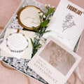 Gift box with spiritual refreshment items, including cards and a bracelet, on a pink background.