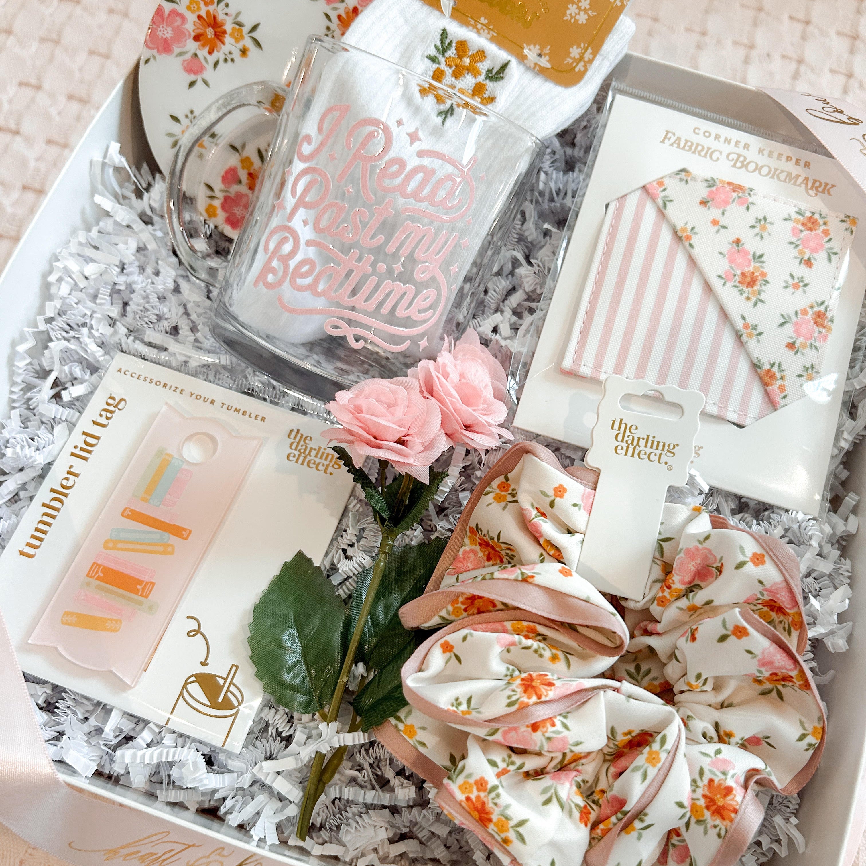Gift box with stationery items including a glass, notebook, and scrunchies on a textured surface.