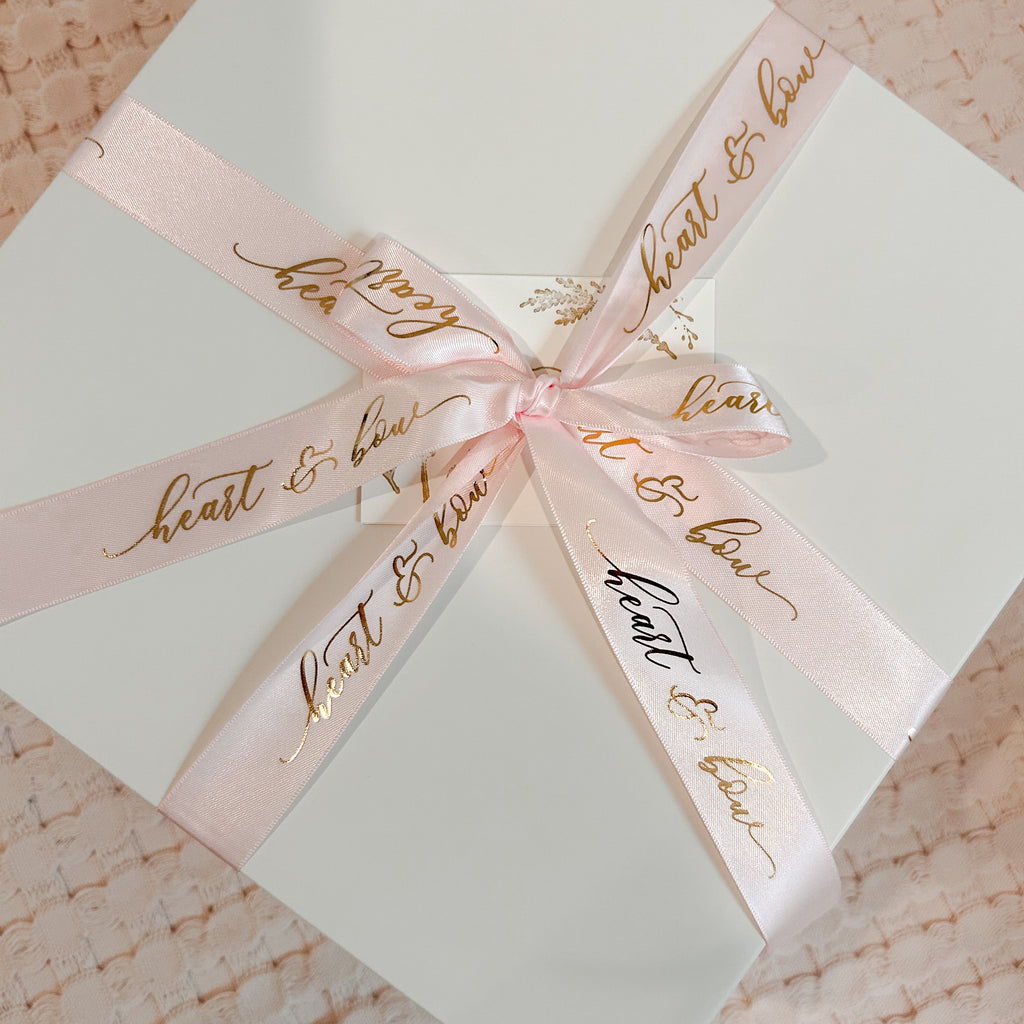 Gift box with a pink ribbon and 'heart & home' text on a textured surface