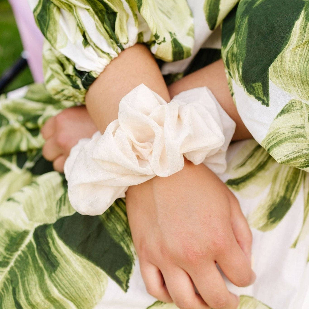 Close-up of a child's hands wearing white scrunchies with a green leafy patterned outfit.