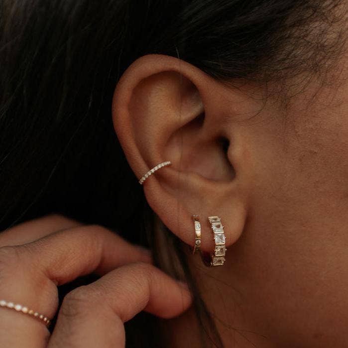 Close-up of an ear with rose gold hoop earrings against a dark background