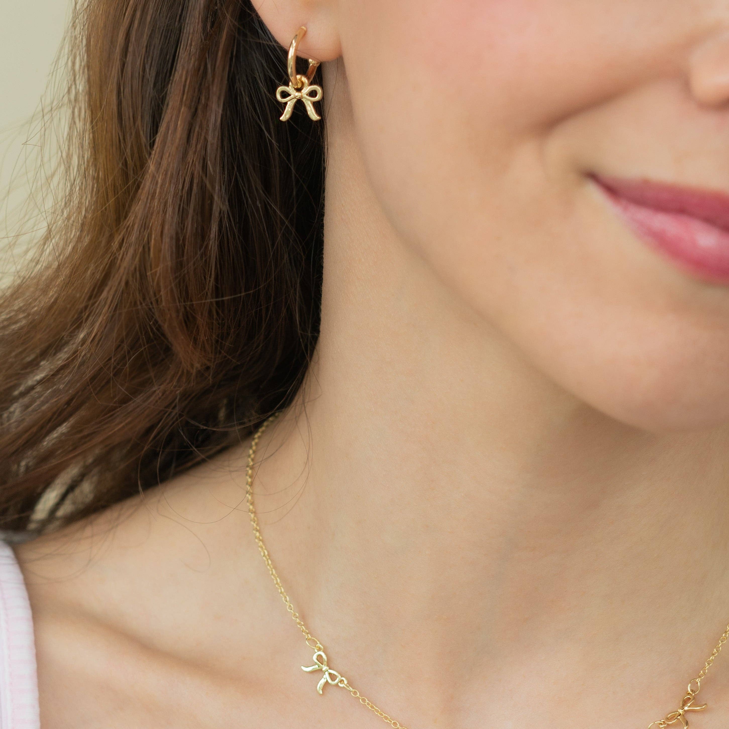 Gold bow-shaped earrings and necklace on a person against a neutral background