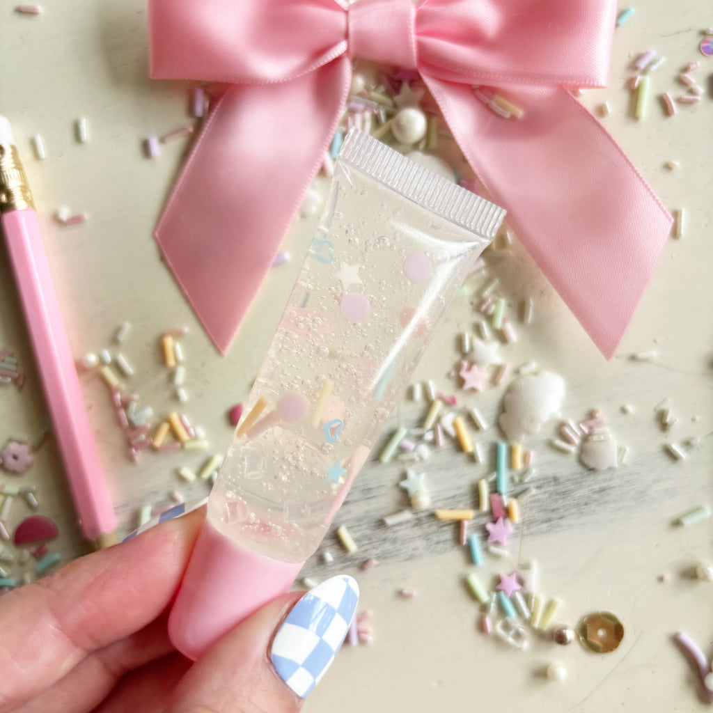 Small pink tube with a bow on top, surrounded by colorful sprinkles.