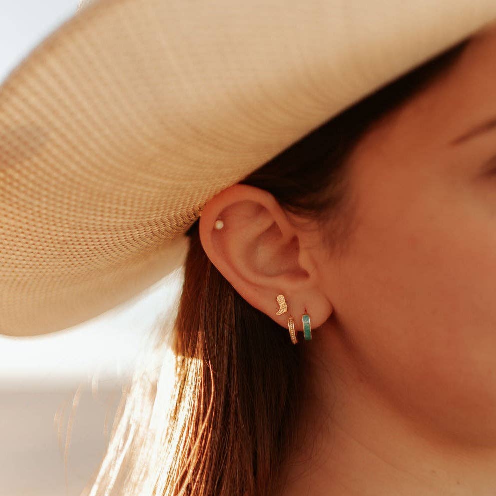 Close-up of a person wearing a beige hat and gold hoop earrings with green stones.