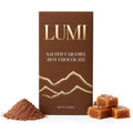 Cocoa powder and caramels: “LUMI salted caramel hot chocolate 3 oz brown and gold box with cocoa powder and salted caramel cubes on white.