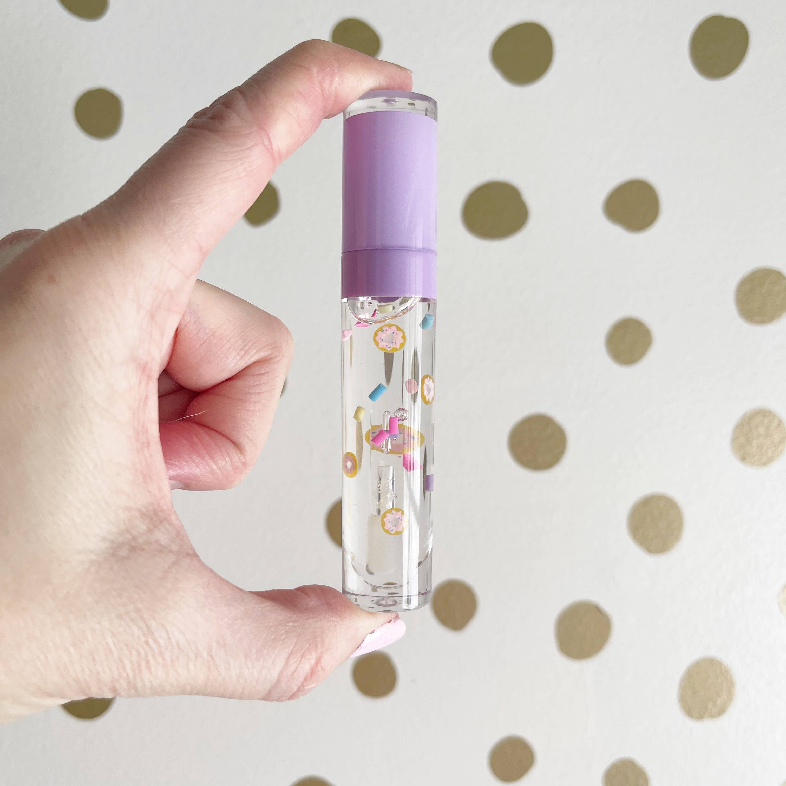 Hand holding a small clear bottle with a purple cap against a polka dot background