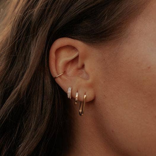 Close-up of an ear with gold hoop earrings and a small stud.
