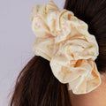 Beige scrunchie with floral pattern on a person's hair against a light gray background