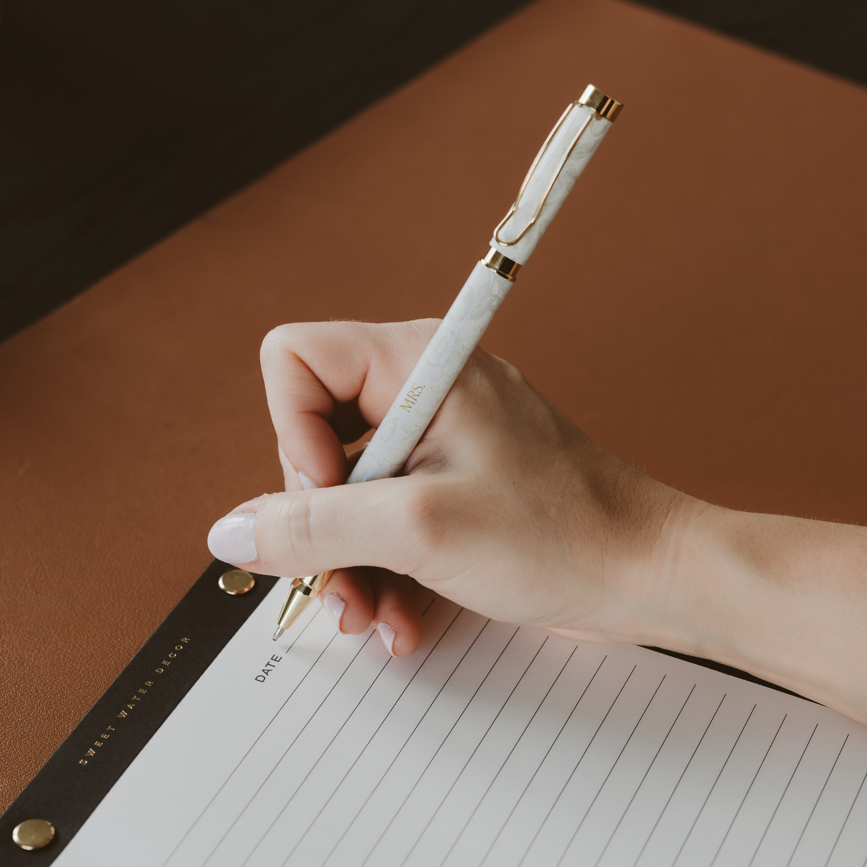 Hand holding a white pen with gold accents on lined paper