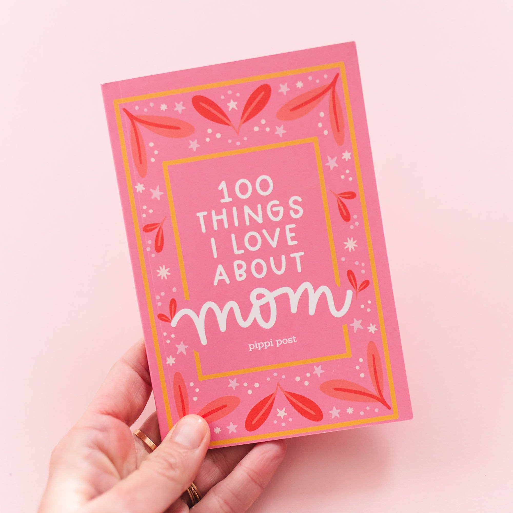 Hand holding the 100 Things I Love About Mom prompted journal with pink illustrated cover.