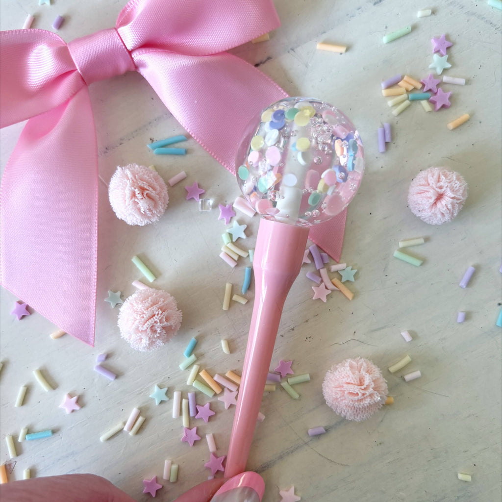 Pink lollipop with a large bow and colorful sprinkles on a light wooden surface.
