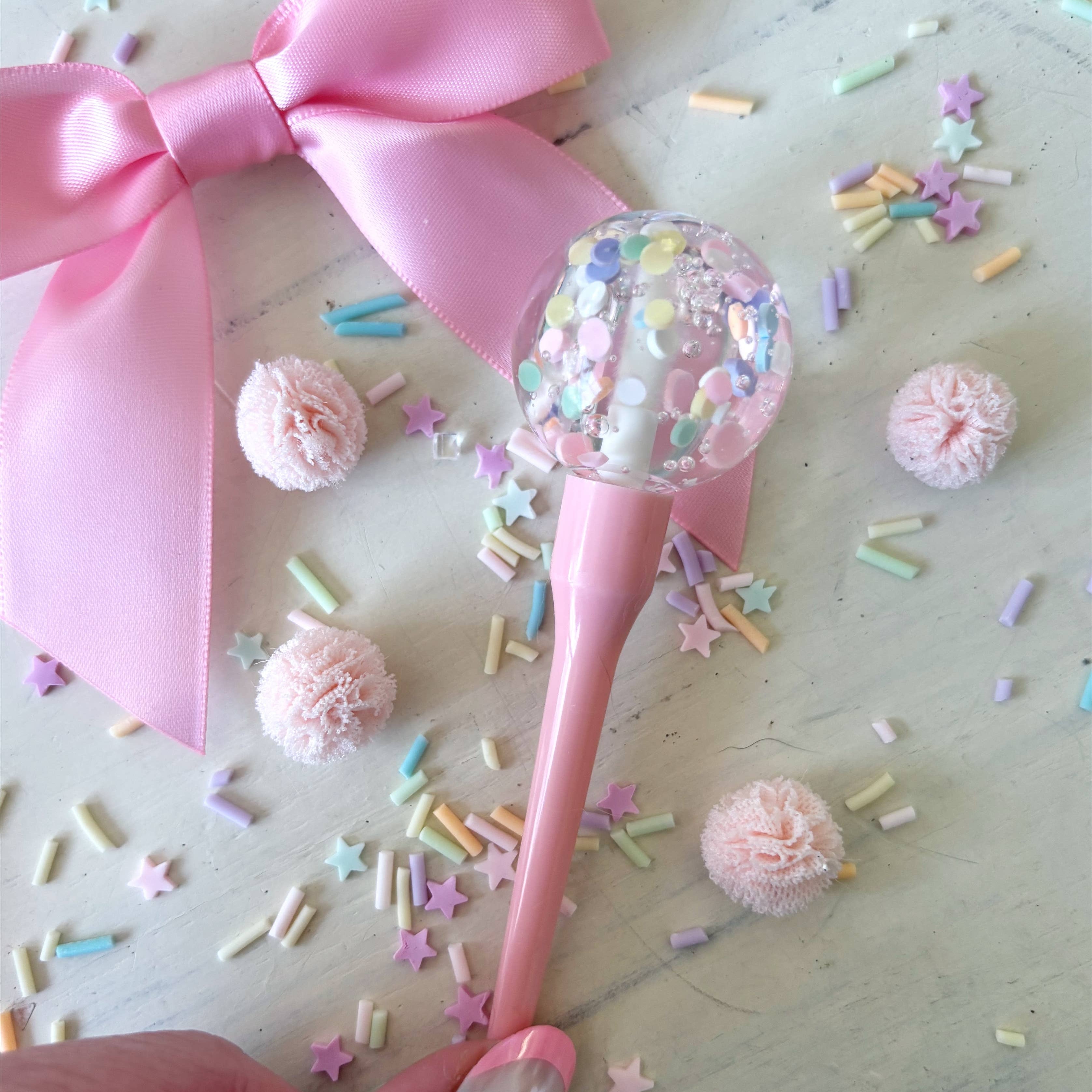 Pink lollipop with a large bow and colorful sprinkles on a light wooden surface.