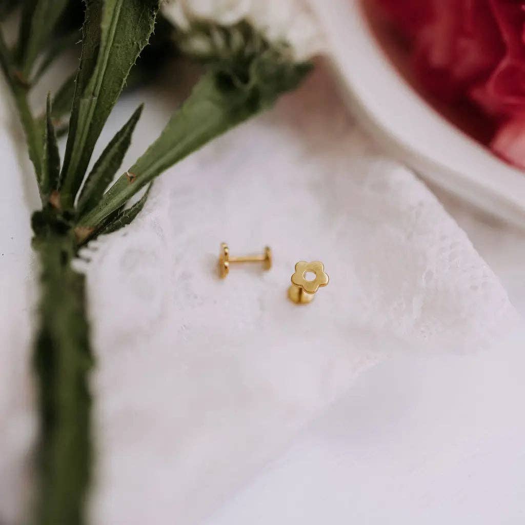 Gold flower-shaped earrings on a white cloth with a blurred background