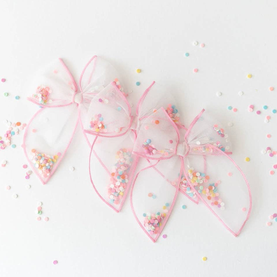 Pink hair bows with colorful sprinkles on a light background