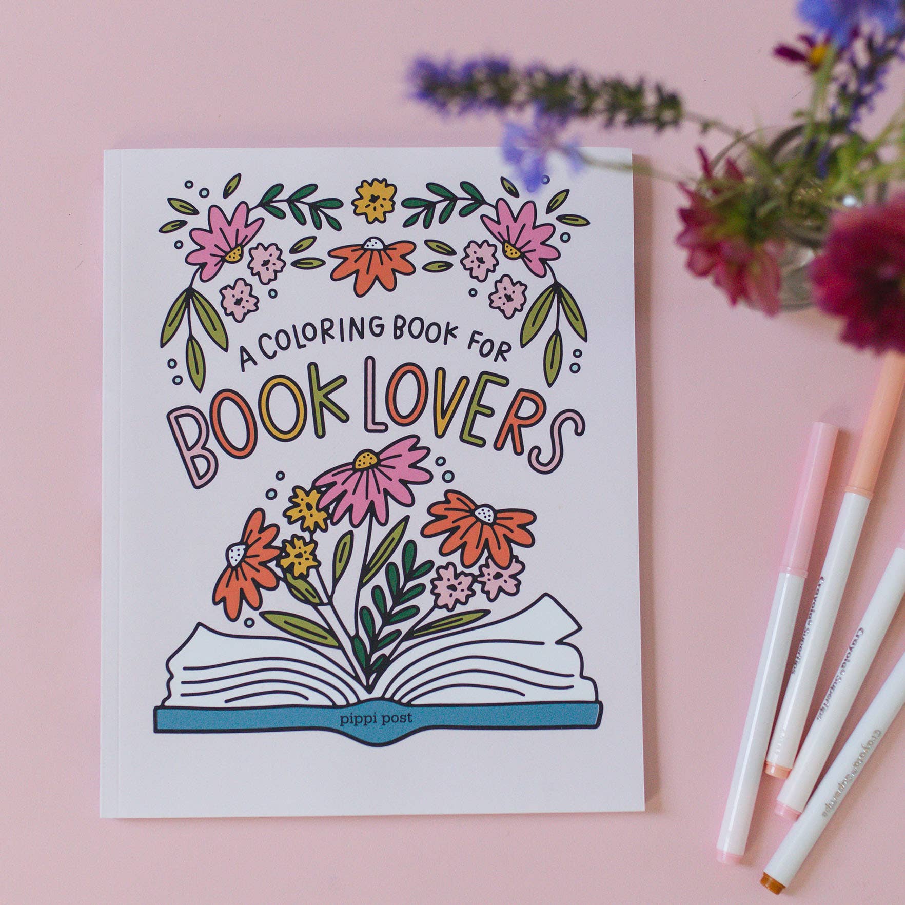 Book Lover Coloring Book displayed with colored pencils and flowers.
