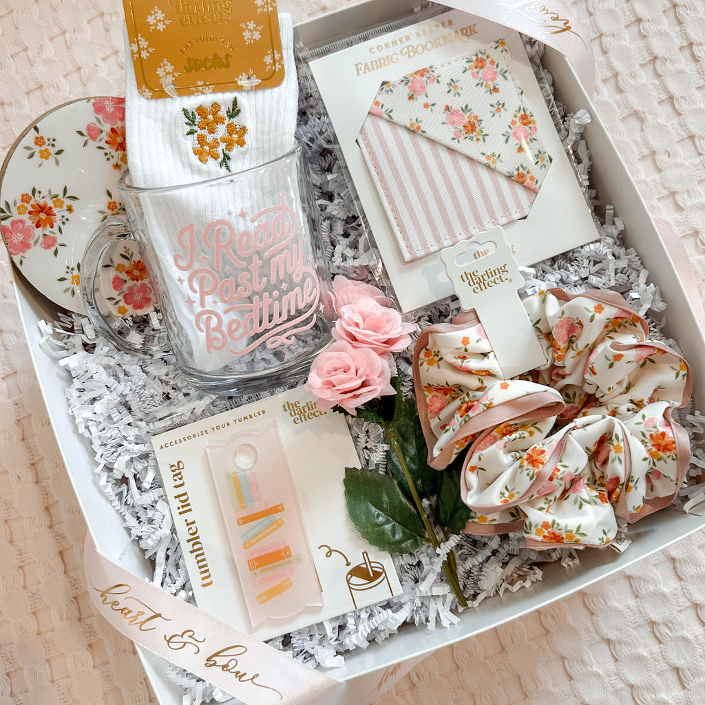 Gift box with stationery items including a mug, notebook, and scrunchies on a textured surface.