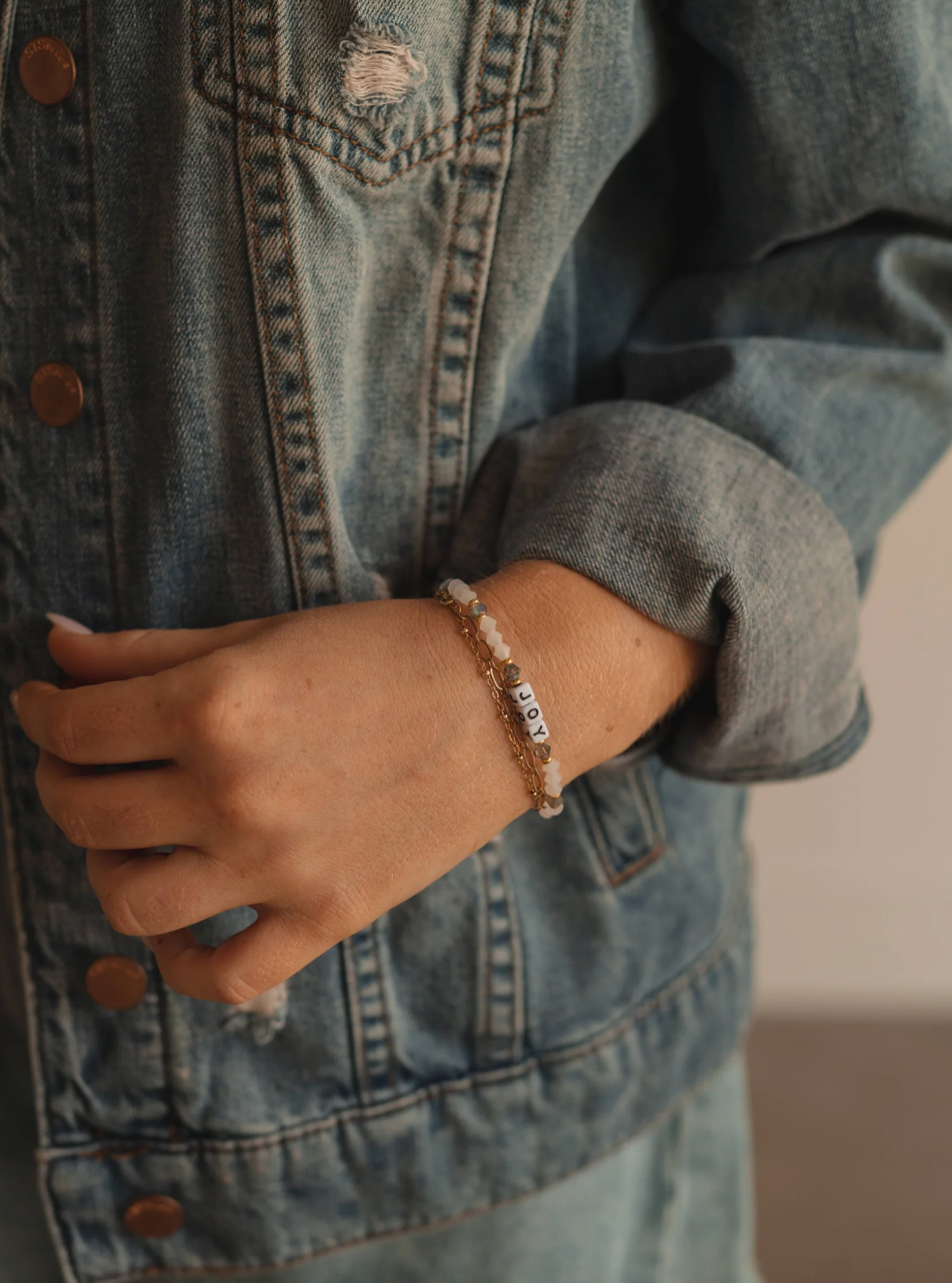 Person wearing a denim jacket with a bracelet on a blurred background