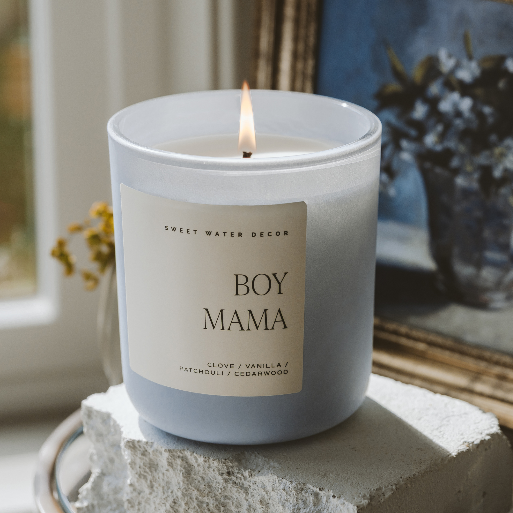 Candle labeled 'BOY MAMA' on a windowsill with a blurred background
