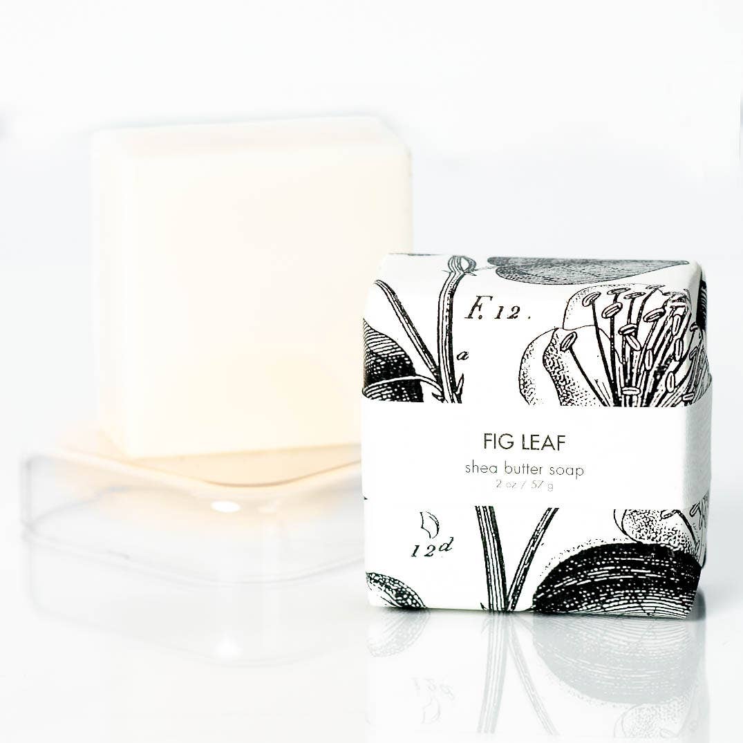 Shea butter soap with 'Fig Leaf' packaging next to a lit candle on a white background