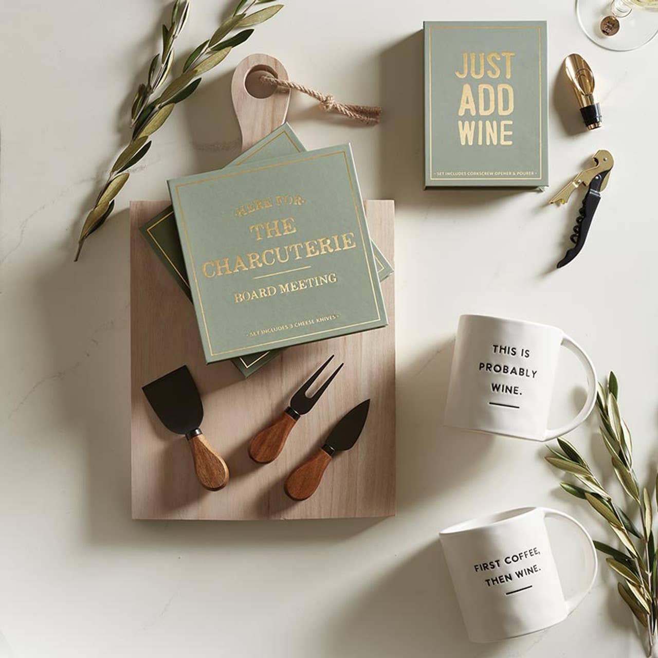Table setting with charcuterie board, wine-themed mugs, and 'Just Add Wine' box on a light surface.